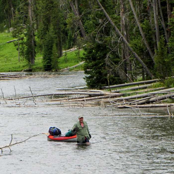 A kayaker walks his kayak up the Lewis River Channel through a section that flows too fast to paddle against. Near Lewis Lake to Shoshone Lake Loop